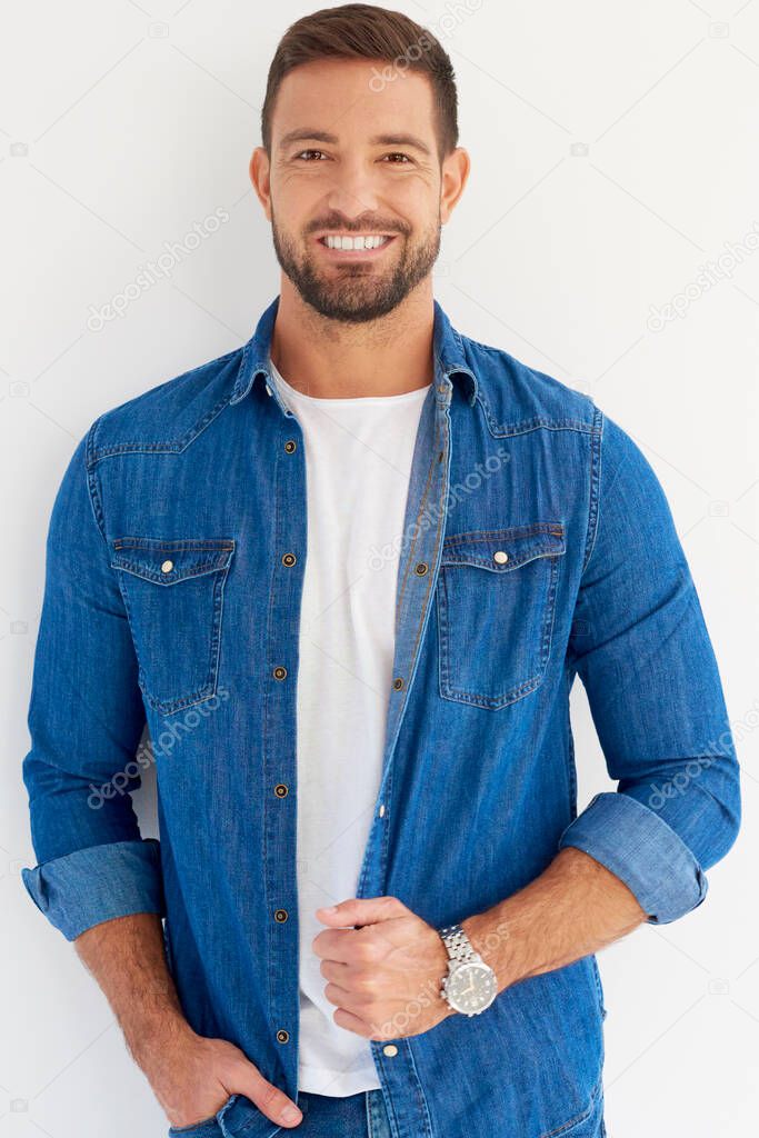 Studio portrait shot of handsome young man standing at isolated white background while looking at camera and smiling. 