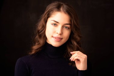 Balıkçı yaka kazak giyen güzel genç bir kadının portresi, ıssız, karanlık arka tarafta dikilirken..