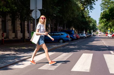 Şehirde yaya geçidinde yürüyen mutlu bir kadının uzun bir görüntüsü..