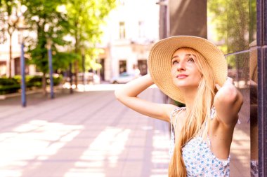 Sokakta dikilirken hasır şapka ve yaz elbisesi giyen çekici genç bir kadının yakın plan portresi.. 