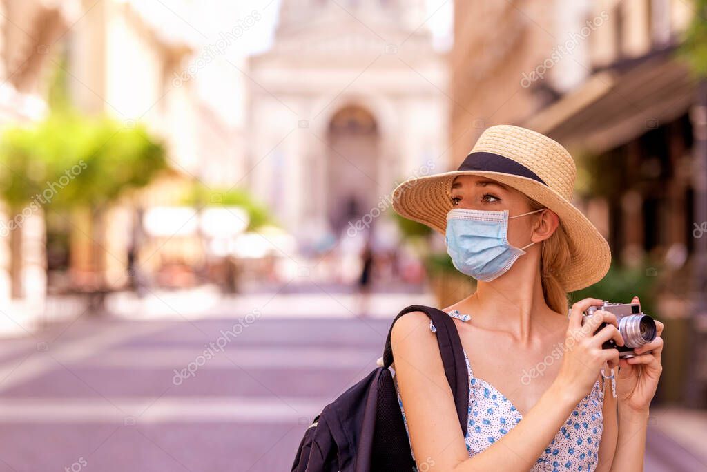 Portrait shot of beautiful blond woman wearing face mask for prevention while using vintage camera to taking photos in the city. 