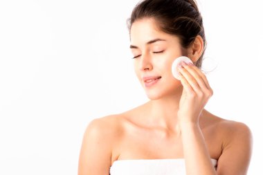 Yüzünü pamukla temizlerken, gözleri kapalı duran güzel bir genç kadının yakın plan fotoğrafı. Beyaz arka planda izole edilmiş. Boşluğu kopyala.