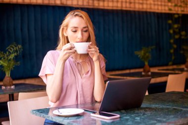 Kafede oturup laptopla çalışırken cappuccinosunu içen çekici bir kadın..
