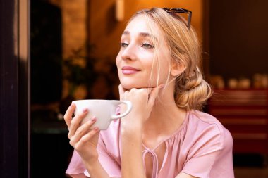 Kafede kahve fincanı tutan ve cappuccino içen güzel bir genç kadının portresi..