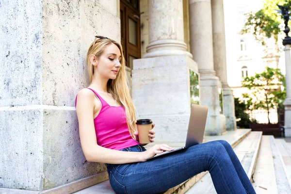 ラップトップとEラーニングを使用しながら キャンパスの階段に座ってコーヒーを飲む女性学生のショット — ストック写真