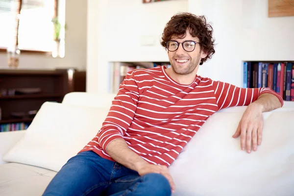 Happy man wearing striped shirt and jeans while relaxing on sofa at home.