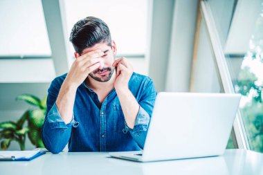 Dizüstü bilgisayarının arkasında otururken gözleri kapalı ve alnında eli olan bir iş adamının başı ağrıyordu..