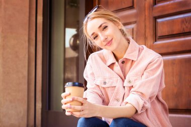 Çekici bir kadın sokakta otururken kahvesini içiyor.