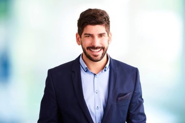 Kapalı alanda durup kameraya bakarken takım elbise giyen genç işadamının yakın plan portresi..