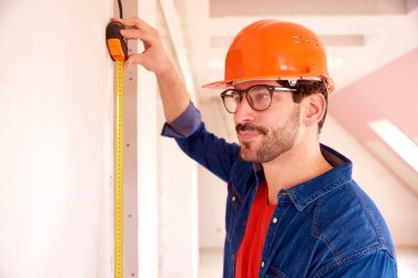 İnşaat alanında çalışırken mezura kullanan genç adamın portresi. 