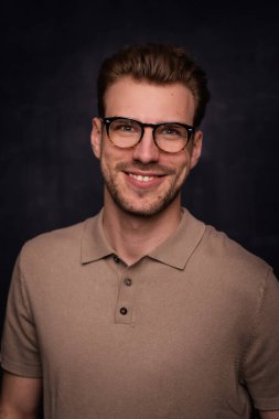 Tecrit edilmiş arka planda duran yakışıklı bir delikanlının yakın çekimi. Uzayı kopyala Tişört ve gözlük takan kendinden emin bir erkek.. 