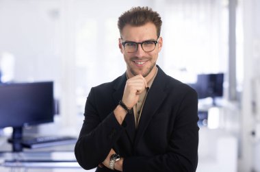 Modern bir ofiste tek başına dururken gülümseyen kendinden emin genç bir iş adamının portresi. Takım elbise ve kravat takan genç bir girişimci. Yakın çekim..