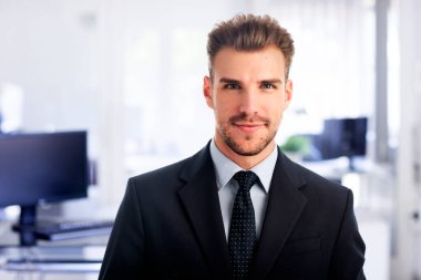 Modern bir ofiste tek başına dururken gülümseyen kendinden emin genç bir iş adamının vesikalığı. Takım elbise ve kravat takan genç bir girişimci. Yakın çekim..