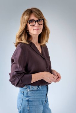 Sarışın kadın, izole edilmiş arka planda duruyor ve kameraya bakıyor. Gömlek ve kot pantolon giyen orta yaşlı bir kadın. Boşluğu kopyala. 