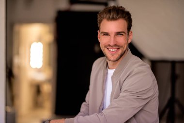 Kameraya bakıp gülümseyen genç bir adamın vesikalığı. Beyaz gömlek ve ceket giyen ve içeride duran kendine güvenen bir adam.. 