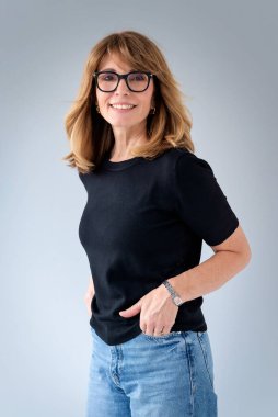 Sarışın kadın, izole edilmiş arka planda duruyor ve kameraya bakıyor. Orta yaşlı kadın kazak ve kot pantolon giyiyor. Boşluğu kopyala. 