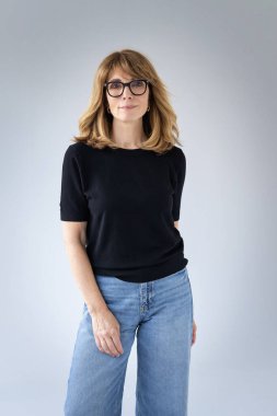 Sarışın kadın, izole edilmiş arka planda duruyor ve kameraya bakıyor. Orta yaşlı kadın kazak ve kot pantolon giyiyor. Boşluğu kopyala. 