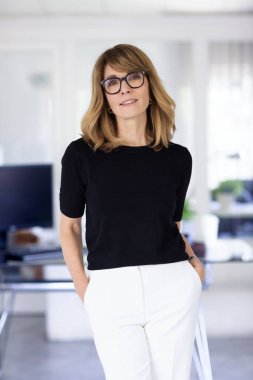 Ofiste kendine güvenen ve kameraya bakan bir iş kadını. Orta yaşlı profesyonel kadın iş kıyafeti giyiyor ve gülümsüyor. Boşluğu kopyala. 