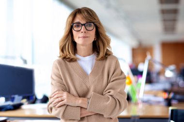 Ofiste kendine güvenen ve kameraya bakan bir iş kadını. Orta yaşlı profesyonel kadın iş kıyafeti giyiyor ve gülümsüyor. Boşluğu kopyala. 