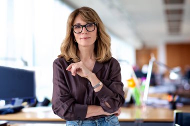 Ofiste kendine güvenen ve kameraya bakan bir iş kadını. Orta yaşlı profesyonel kadın iş kıyafeti giyiyor ve gülümsüyor. Boşluğu kopyala. 