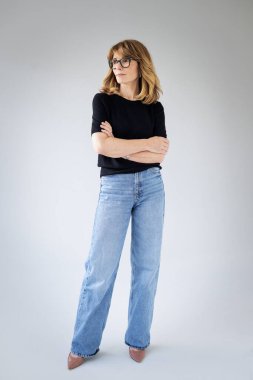 Sarışın kadın, izole edilmiş arka planda güvenle ayakta duruyor ve başka tarafa bakıyor. Siyah kazak ve kot pantolon giyen orta yaşlı bir kadın. Uzayı kopyala Tam uzunluk. 