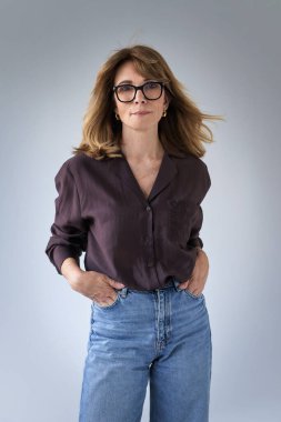 Sarışın kadın, izole edilmiş arka planda duruyor ve kameraya bakıyor. Gömlek ve kot pantolon giyen orta yaşlı bir kadın. Boşluğu kopyala. 