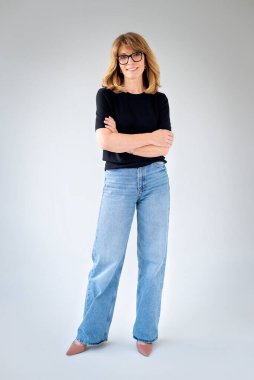 Sarışın kadın, izole edilmiş arka planda duruyor ve kameraya bakıyor. Siyah kazak ve kot pantolon giyen orta yaşlı bir kadın. Uzayı kopyala Tam uzunluk. 