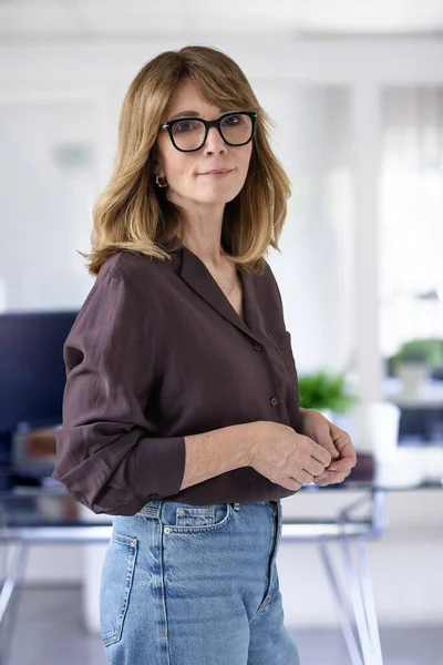 Ofiste kendine güvenen ve kameraya bakan bir iş kadını. Orta yaşlı profesyonel kadın iş kıyafeti giyiyor ve gülümsüyor. Boşluğu kopyala. 