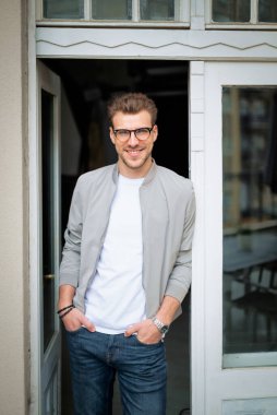 Kameraya bakıp gülümseyen genç bir adamın vesikalığı. Beyaz gömlek ve ceket giyen ve kapının yanında duran kendine güvenen bir adam.. 