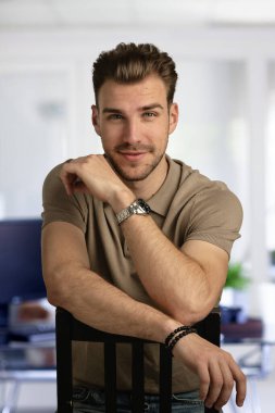 Modern bir ofiste tek başına otururken gülümseyen kendinden emin genç bir iş adamının vesikalığı. Gündelik kıyafetler giyen genç bir girişimci. Yakın çekim..