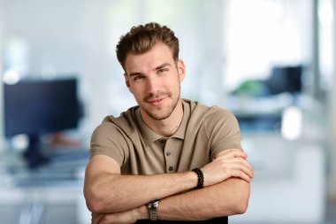 Modern bir ofiste tek başına otururken gülümseyen kendinden emin genç bir iş adamının vesikalığı. Gündelik kıyafetler giyen genç bir girişimci. Yakın çekim..