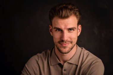 Tecrit edilmiş arka planda oturan yakışıklı bir gencin yakın çekimi. Uzayı kopyala Polo tişört giyen ve kameraya gülümseyen kendinden emin bir erkek..