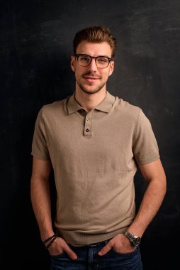 Tecrit edilmiş arka planda duran yakışıklı bir delikanlının yakın çekimi. Uzayı kopyala Polo gömlek ve gözlük takan kendinden emin bir erkek.. 