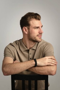 Tecrit edilmiş arka planda oturan yakışıklı bir gencin yarı profili. Kendine güvenen erkek polo gömlek giyiyor ve başka tarafa bakıyor. Uzayı kopyala İzole edilmiş arka plan, stüdyo çekimi..