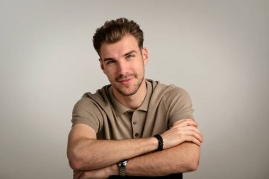 Tecrit edilmiş arka planda oturan yakışıklı bir gencin stüdyo fotoğrafı. Polo tişört giyen ve kameraya bakan kendinden emin bir erkek. Uzayı kopyala İzole edilmiş arkaplan.