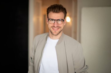 Kameraya bakıp gülümseyen genç bir adamın vesikalığı. Beyaz gömlek ve ceket giyen ve içeride duran kendine güvenen bir adam.. 