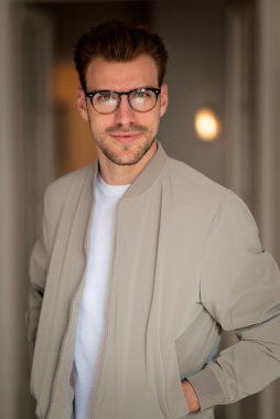 Kameraya bakıp gülümseyen genç bir adamın portresi. Beyaz gömlek ve ceket giyen ve içeride duran kendine güvenen bir adam.. 