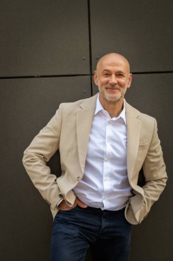 Gri bir duvarın önünde caddede duran orta yaşlı bir adam. İş kıyafeti giymiş yakışıklı bir iş adamı.. 