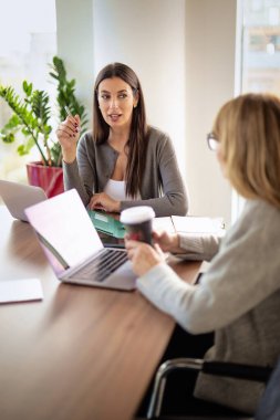Takım çalışması ve işbirliği konsepti. Toplantı odasında dizüstü bilgisayarda birlikte çalışan iki bayan meslektaşım. Bir grup iş adamı tartışıyor.. 