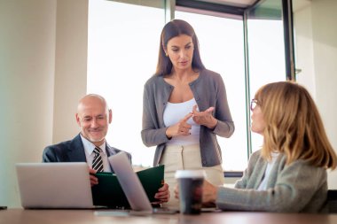Takım çalışması ve işbirliği konsepti. Toplantı odasında dizüstü bilgisayarda birlikte çalışan bir erkek ve iki bayan iş arkadaşı. Bir grup iş adamı tartışıyor.. 