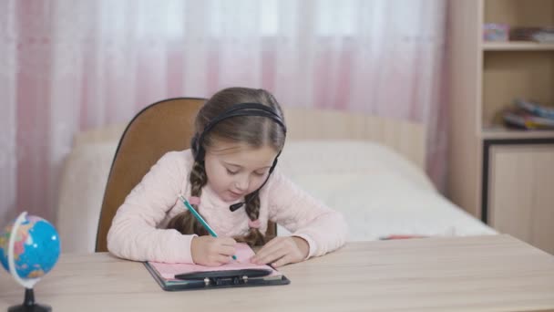 Κοριτσάκι με ακουστικά που κάθεται στο τραπέζι — Αρχείο Βίντεο