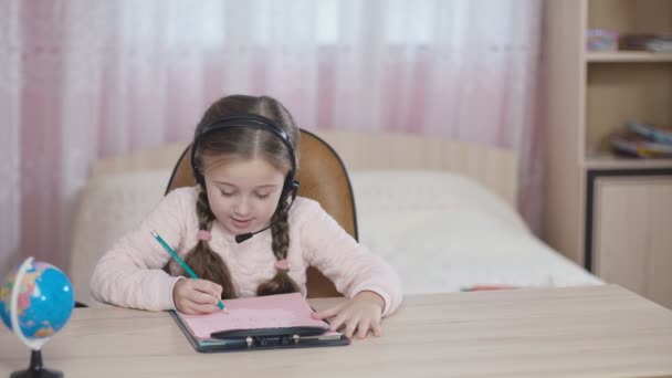 Dziewczynka z słuchawki siedzi przy stole — Wideo stockowe
