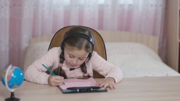 Niña con auriculares sentada en la mesa — Vídeos de Stock