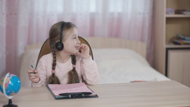 Menina com fones de ouvido sentado à mesa — Vídeo de Stock