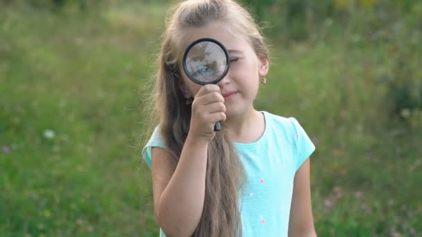 Little girl looks through a magnifying glass — Stock Video