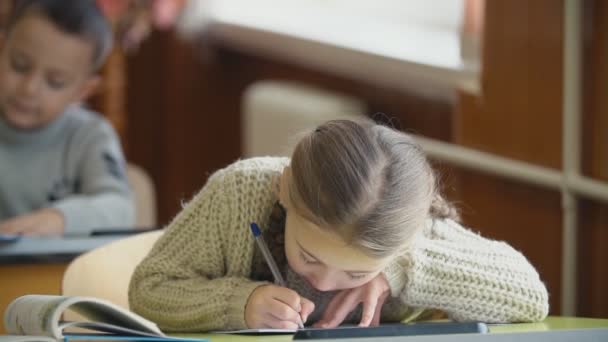 A menina escreve enquanto se senta em sua mesa — Vídeo de Stock