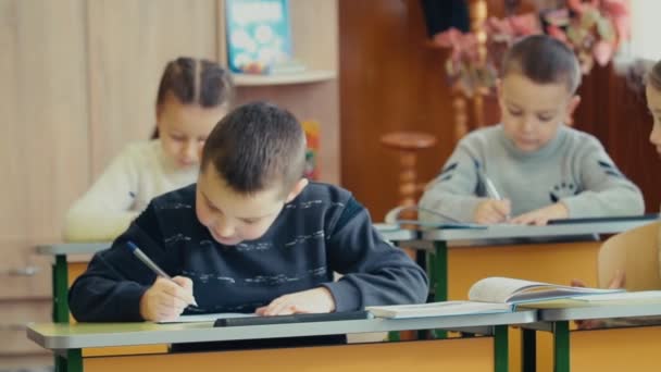 Los niños escriben sentados en un escritorio — Vídeo de stock