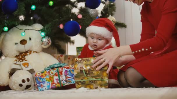Mutter mit Baby im Weihnachtsmannkostüm schaut sich Geschenke an — Stockvideo