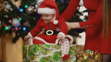 Anne bebek bakarak santa kostüm ile Noel ağacının altında sunar
