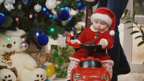 サンタのスーツの小さな女の子がおもちゃの車に転がり — ストック動画